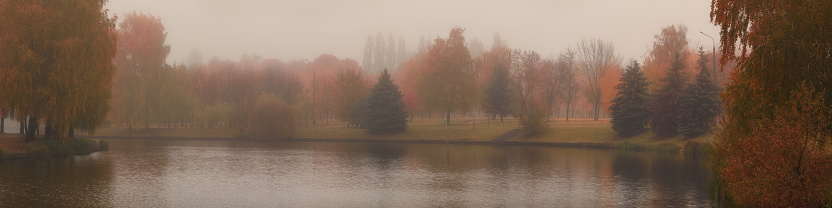 multicolor of late autumn. morning foggy city park with lush foliage along the river. beautiful widescreen panoramic side view with natural atmospheric blur. format 20x5