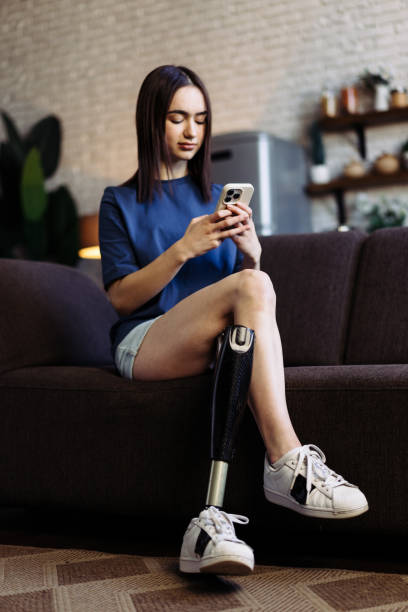 istock Woman with disability sits on sofa typing messages on phone 1825305790