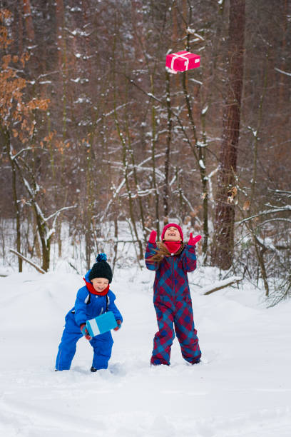Happy children in a winter snow-covered forest with gift boxes. Christmas fun for Christmas and New Year.