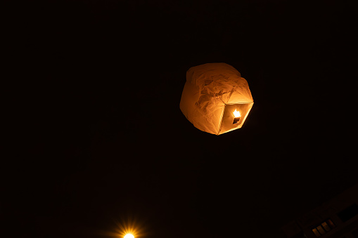 orange chinese lantern flying in the sky and a streetlamp below illuminate the sky of pamplona navarre