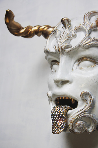 White face of the mythological creature. Detail of the statue, gilded rococo decoration, tongue decorated with zircons. Contemporary art.