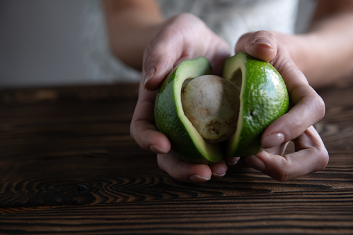 Young woman holding halves of avocado