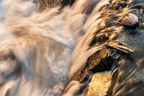 Abstract details of water movemet,at sunset.Sunlight shining on rocks,next to blurred motion of the river,rushing by,at the main waterfalls and rapids of Don Khon island.