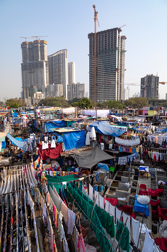 This image captures the bustling activity of the Dhobi Ghat, Mumbai's famous open-air laundromat. Known as the world's largest outdoor laundry, Dhobi Ghat presents a unique aspect of the city's daily life. The photograph showcases rows of concrete wash pens, each fitted with its own flogging stone, where dhobis (washermen and women) vigorously wash a vast array of clothes and linens. The vibrant scene is filled with lines of laundry drying under the sun, creating a colorful mosaic that is both functional and visually striking. The image aims to highlight this traditional laundry method, showcasing the hard work and community spirit of the dhobis, while offering a glimpse into a unique, lesser-seen side of urban life in Mumbai.