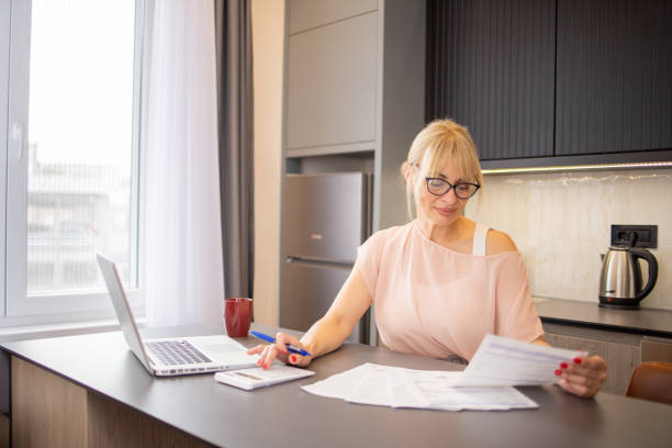 istock Mature woman using calculator while going through bills and home finances 1825500859