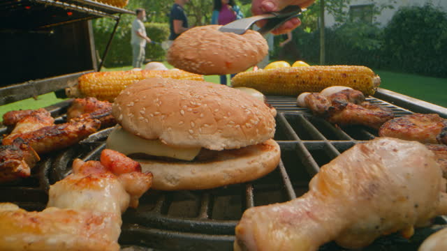 DS person placing the burger buns on top of burgers on the grill at a garden party