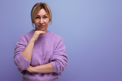 portrait of charming cute blondie woman in casual sweater on purple background with copy space.
