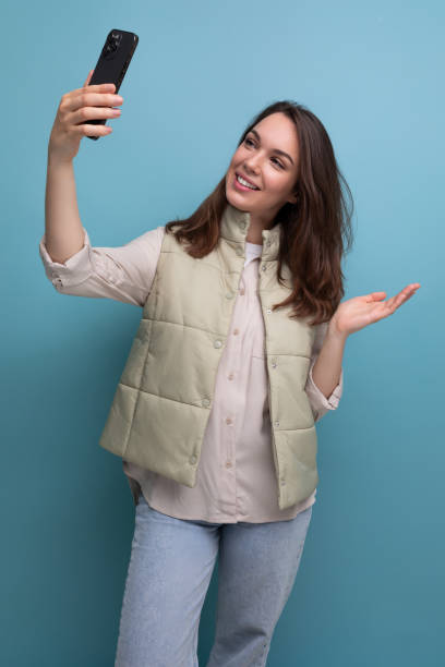 istock brunette young woman taking selfie using mobile phone on studio background 1825518968