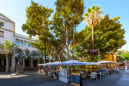 Lush trees and sidewalk cafes outside St Francis Church at Plaza de San Francisco in Santa Cruz de Tenerife Spain, on the Canary island of Tenerife, Spain.