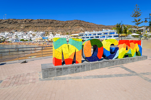 The colorful letters and text welcome sign for the picturesque, whitewashed fishing village of Puerto de Mogan, Spain, on the island of Gran Canaria.