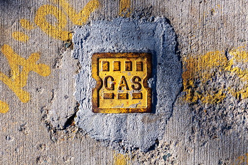 Old rusted yellow iron cover of a gas pipeline in a damaged concrete sidewalk. Yellow spray paint on the sidewalk.