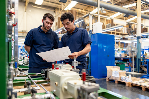 Team of Latin American workers assembling water pumps at a factory and looking at blueprints -  production line concepts