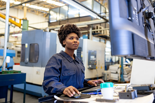 African American female employee operating a machine at a manufacturing factory using a computer - production line worker