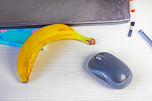 banana on the desktop near the computer mouse and laptop. Narbote snack and ideas