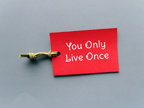Red tag with text written You Only Live Once - concept of YOLO - ideology is an encouragement to seize the day, to go for it, live your best life now