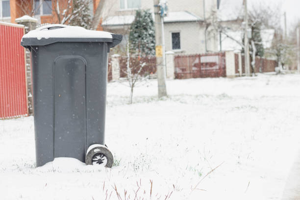 A trash can covered with snow next to a house. Garbage removal in winter