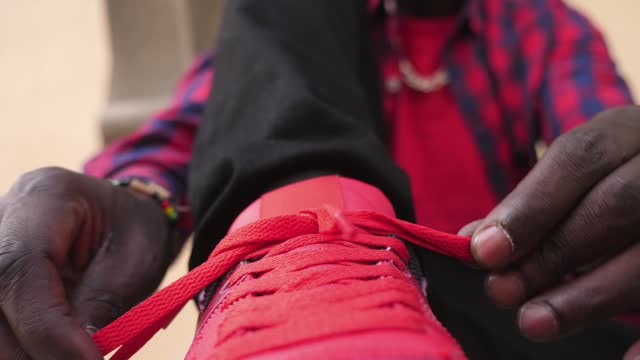 detail of the hands of a young african man tying his red sneakers