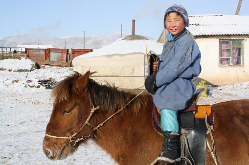 A boy on a Mongol Takhi horse in the serene steppe of Tuv province, Mongolia. A Mongol Takhi horse (Przewalski) is tough for the longer cold winter months in the country.  The steppe is serene and vast.