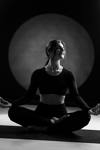 Athletic woman doing yoga in the studio and posing against the backdrop of light illuminations in the background. Yoga and meditation concept