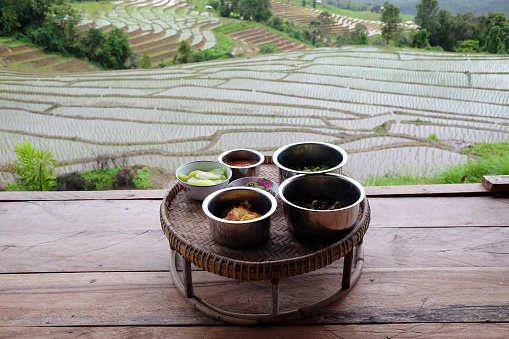 Kantoke, Kind of wooden utensil in northern of Thailand for put the foods to serve on terrace of homestay and Paddy rice fields on mountain in rainy season in countryside. Food and travel concept