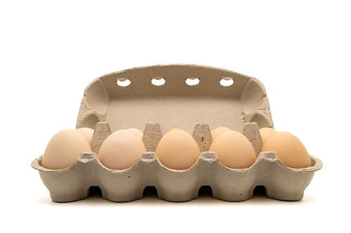 Cardboard egg box with ten chicken eggs isolated on white background with copy space. Side view.