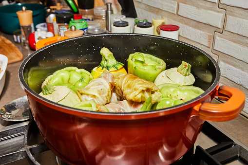 Stuffed zucchini and peppers are cooked in a saucepan on a gas stove.