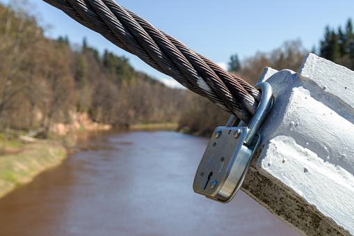 metal key hooked and locked on metal rope with river and tree background