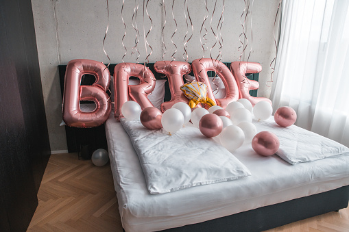 In the intimate setting of a hotel room, charming balloon decorations for the bride create a delightful and elegant display on the bed.