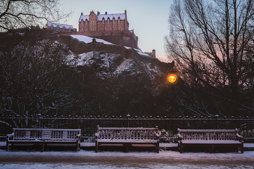 View of a snow covered Edinburgh Castle with empty park benches at Princes Street Gardens on a winter morning in the historic old town of Edinburgh, Scotland, UK.