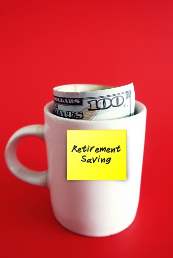 A yellow sticky note written RETIREMENT SAVING on white ceramic cup with cash dollars money inside, isolated on red background. Concept of setting money savings goal for retirement