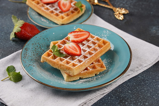 Belgian waffles with fresh strawberries, sugar powder and mint leaves