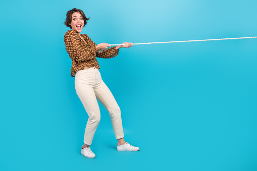 Photo of amazed positive girl pull string playing tug war game isolated blue color background.