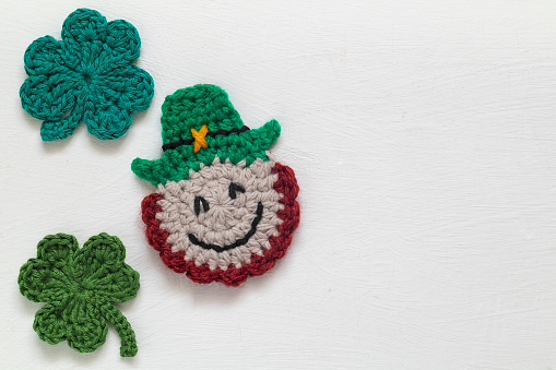 Handmade crochet St Patrick's day leprechaun and clover shamrock close up on a white background. Top view. Copy space.