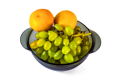 Ripe green grapes and two tangerines in a plate on a white background.