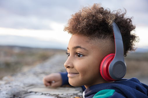 Joyful child listening to music with red headphones, and looking to the horizon.  The rhythmic beats of the music create a cheerful atmosphere as the child embraces the joy of the moment.