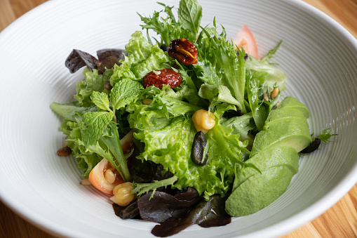 A plate of salad comprising fresh greens, black olives, berries, tomatoes, avocado,chick peas and pine nuts.