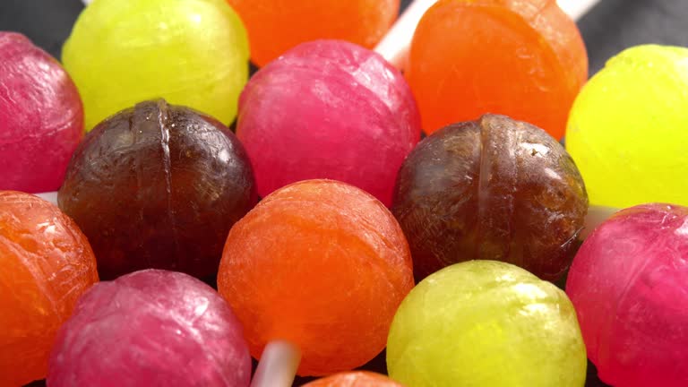 Colorful lollipops or candy bonbons on a stick rotating on black plate in macro top view sun light. Holiday sweet treats. Delicious sweets and candies for children