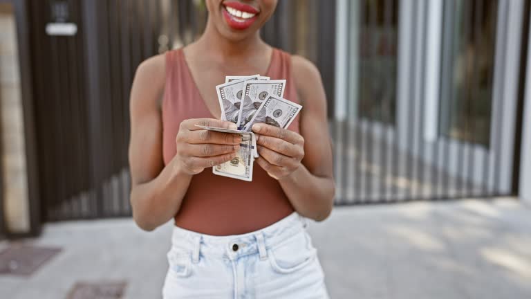 Confident african american woman joyfully counts her dollars with a beautiful smile on the sunny city street