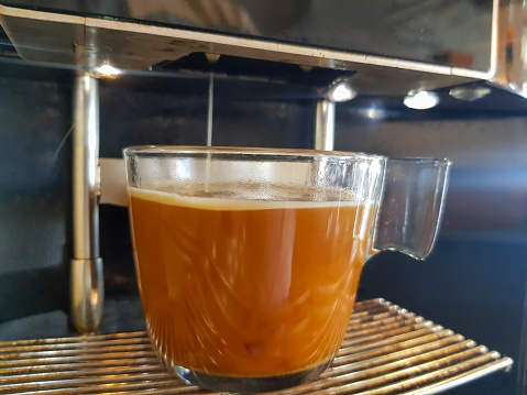 glass cup of coffee filled by machine with cream topping and hot steam