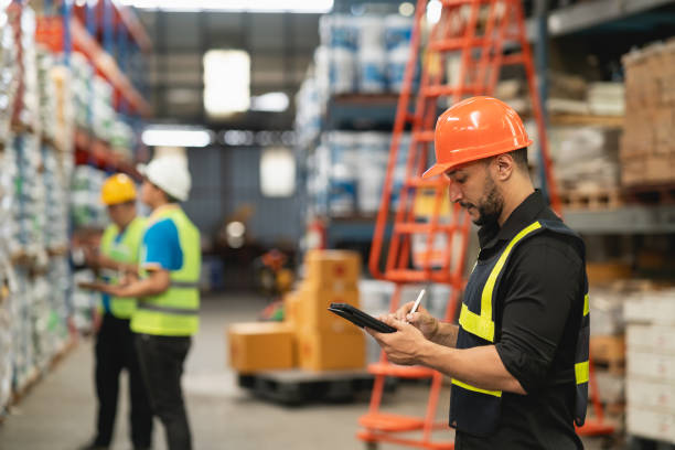 istock Professional manager man employee using tablet check stock working at warehouse. Worker wearing high visibility clothing and a hard hat, helmet and checking and count up goods or boxes for delivery. 1826554074