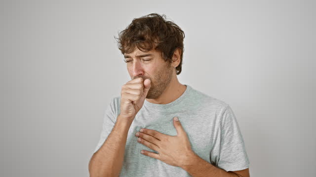 Young man in casual t-shirt coughing, a distressing sign of cold, bronchitis or worse! health care alert on an isolated white background.