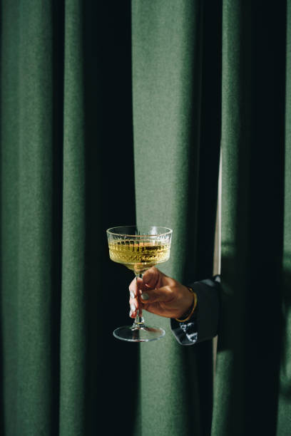 elegant woman toasting with champagne flute from behind the curtain - frisdrank-fotos stockfoto's en -beelden