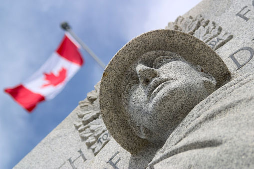War monument with Canadian flag waving against graduated blue sky.
