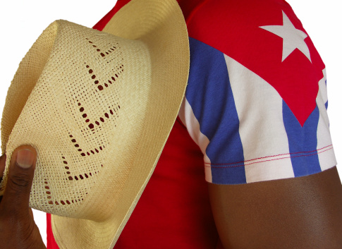 Man holding a Cuban straw hat close to his chest. He is dressed in a t-shirt with a Cuban flag. Close-up