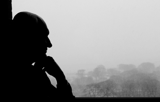 silhouette of older man looking out the window thinking (it's snowing outside)