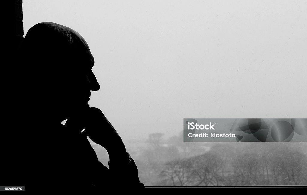 Thinking out the window silhouette of older man looking out the window thinking (it's snowing outside) In Silhouette Stock Photo