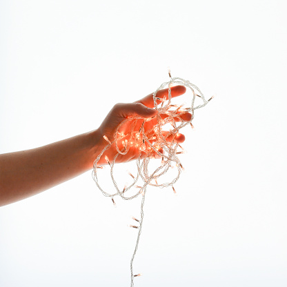 Close up of woman hands holding string Christmas light on white background. Gesture of getting ready for New Years eve. Gentle motion and gesture female hands.