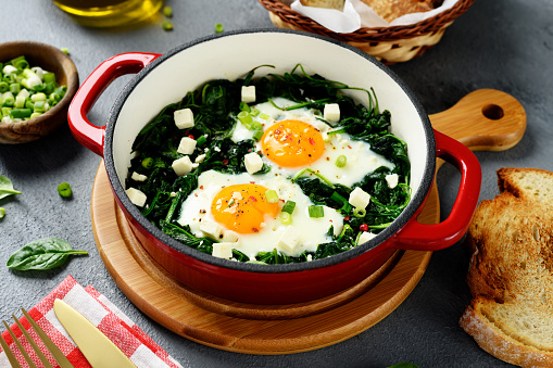 Green shakshuka with fresh spinach, fried eggs and feta cheese cubes, healthy breakfast.