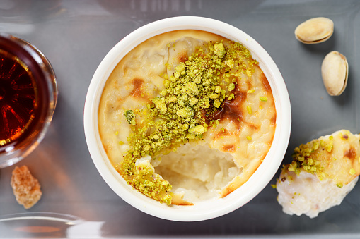 Baked rice pudding- traditional turkish milk dessert, served with pistachio nuts and cup of black tea. top view