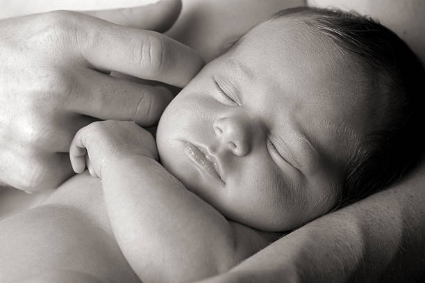 Black and White Image of Newborn in Father's Loving Arms Black and white image of newborn baby being lovingly held by father.  Closeup headshot. sheltering photos stock pictures, royalty-free photos & images